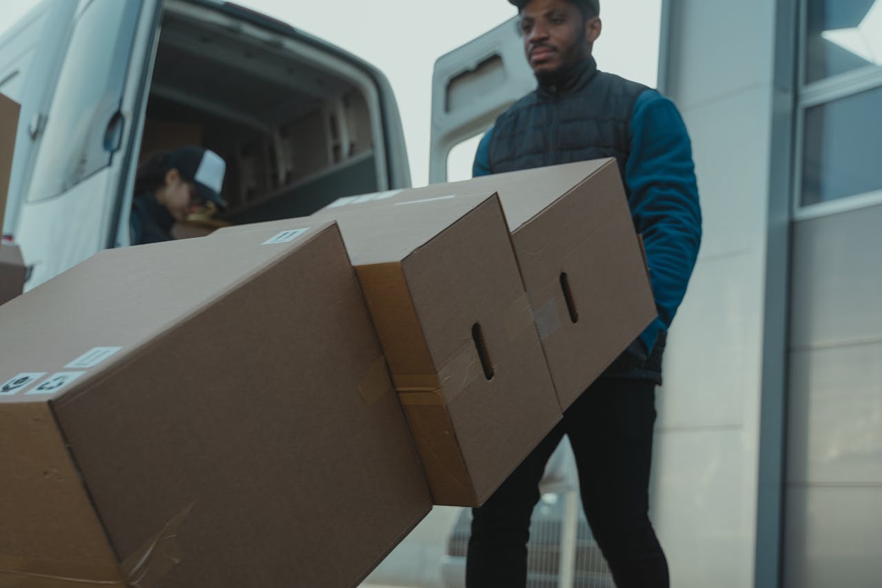 Services Delivery man carrying cardboard boxes from a van outside a modern building.